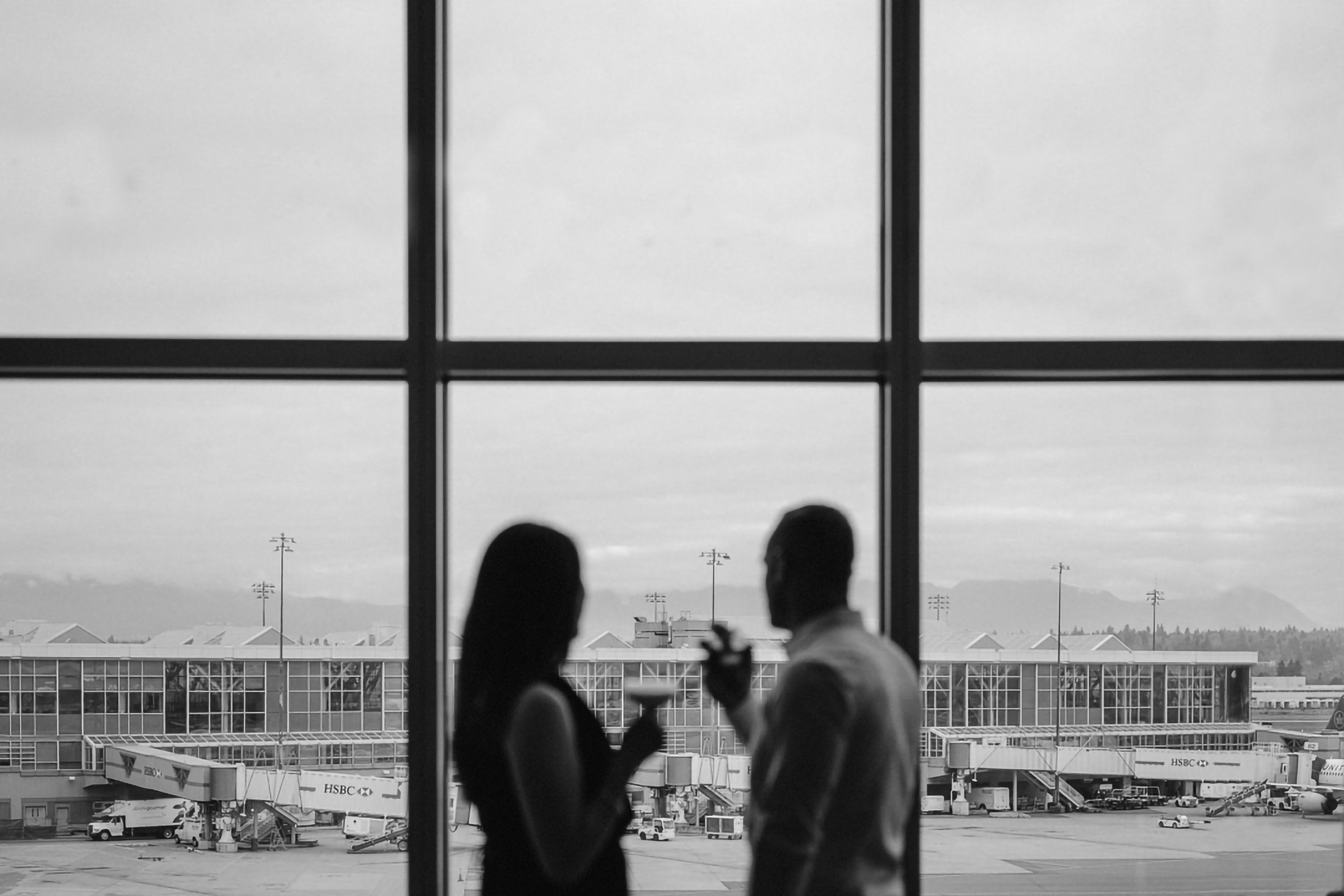 black and white photo of a couple sharing a drink at the lounge while looking out over the airport