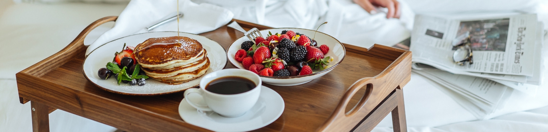woman pouring syrup on her pancakes while eating her breakfast in bed