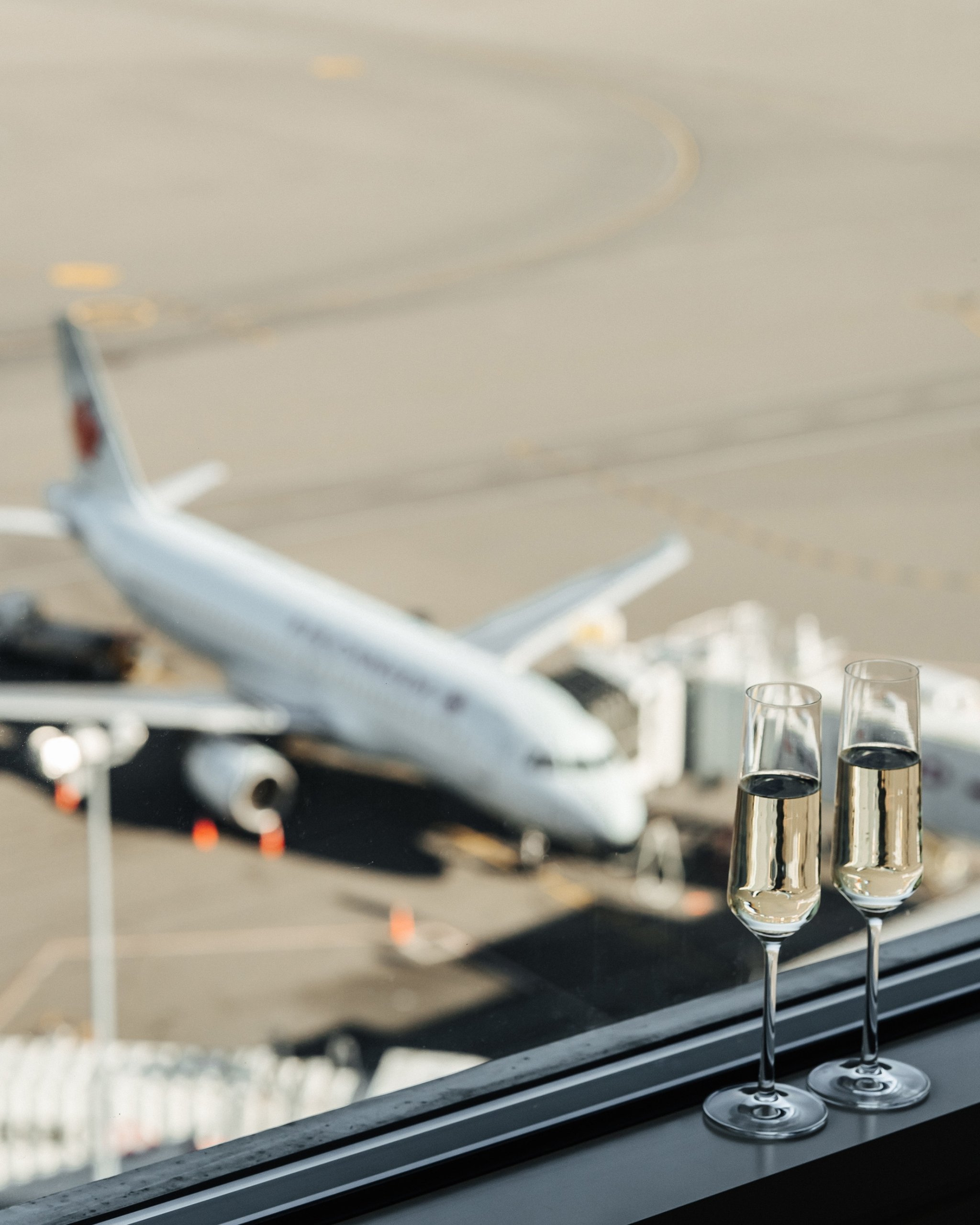 two glasses of wine on a window ledge with a plane in the background
