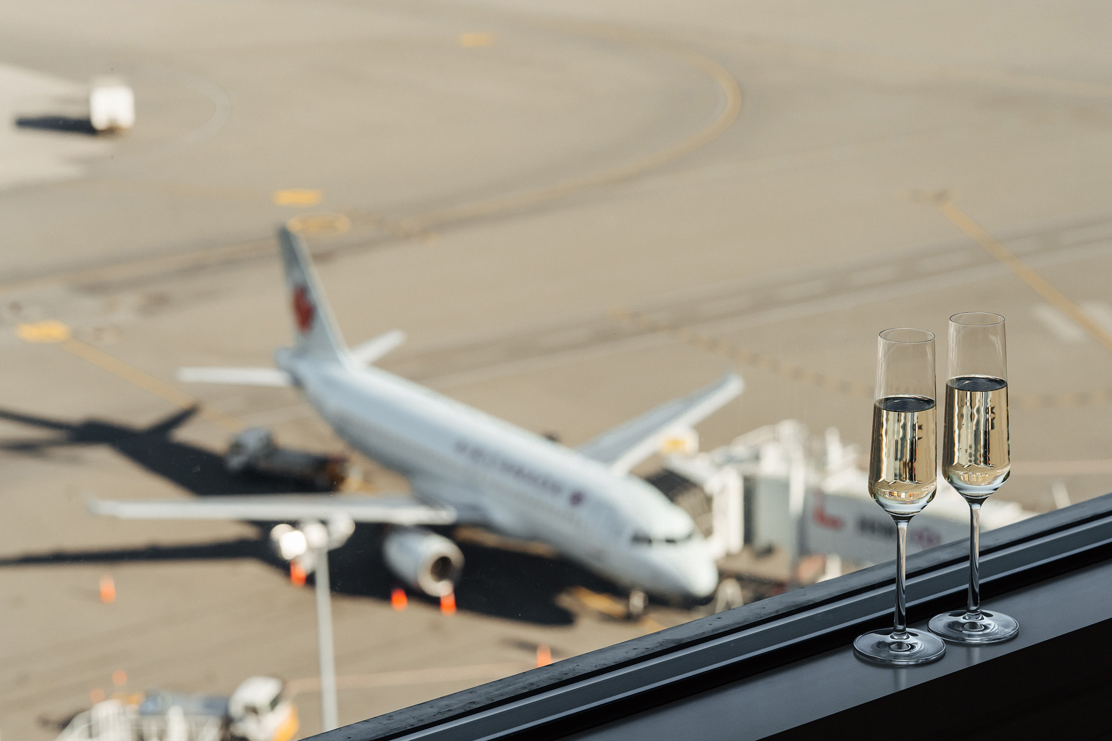 two glasses of wine sitting on a window ledge overlooking an airplane