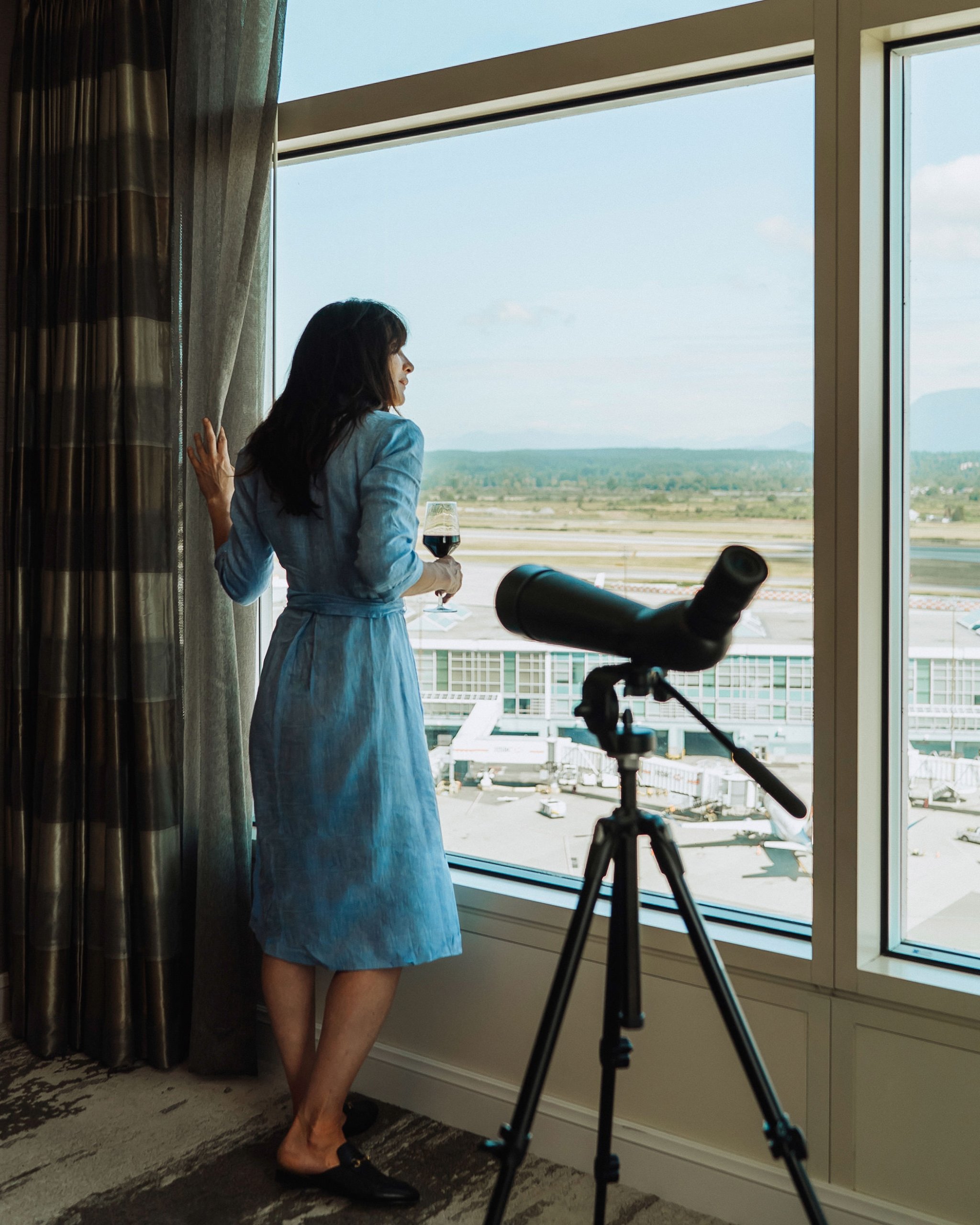 woman with a glass of wine staring out the window watching the planes