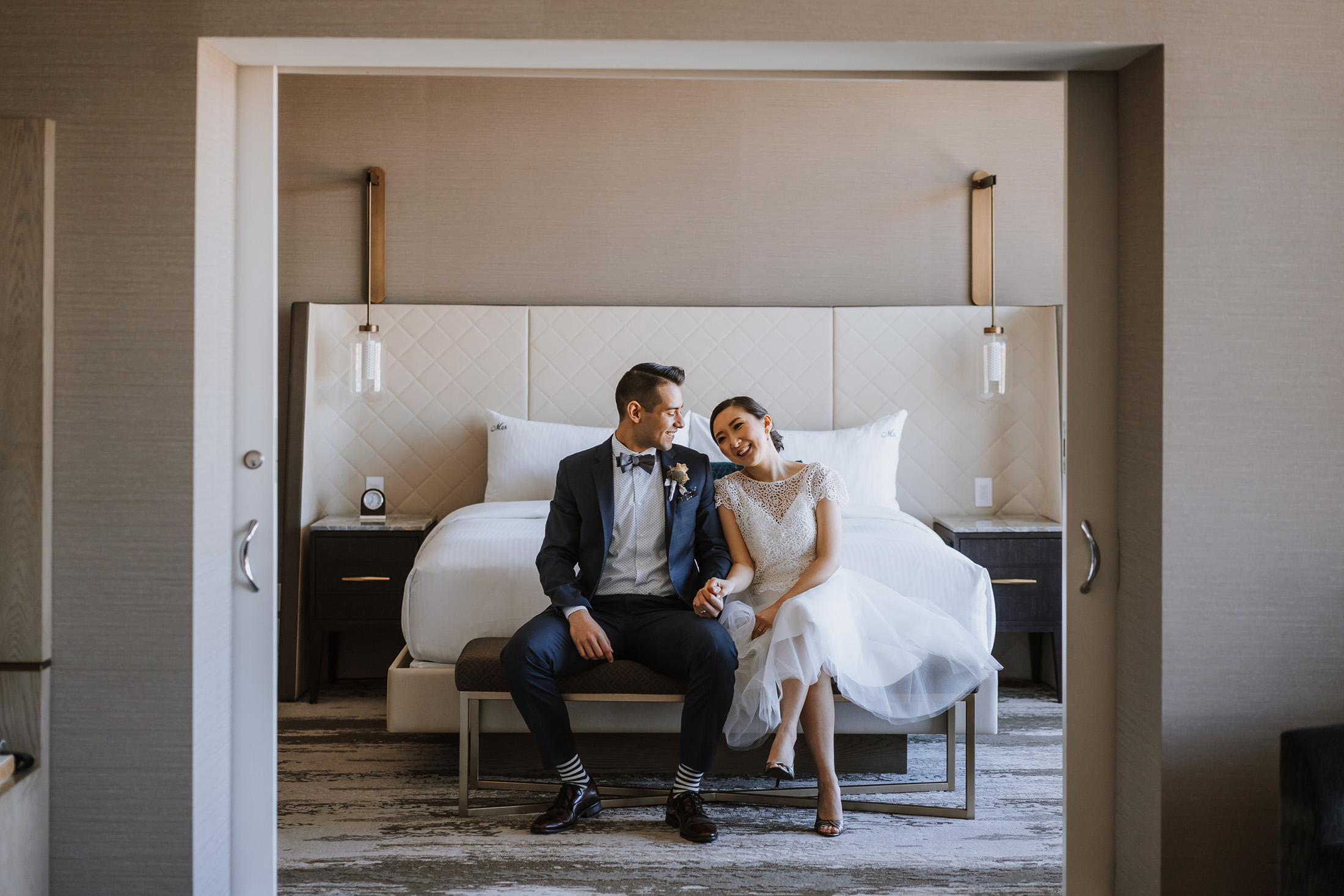 bride and groom sitting on a bench at the foot of the bed