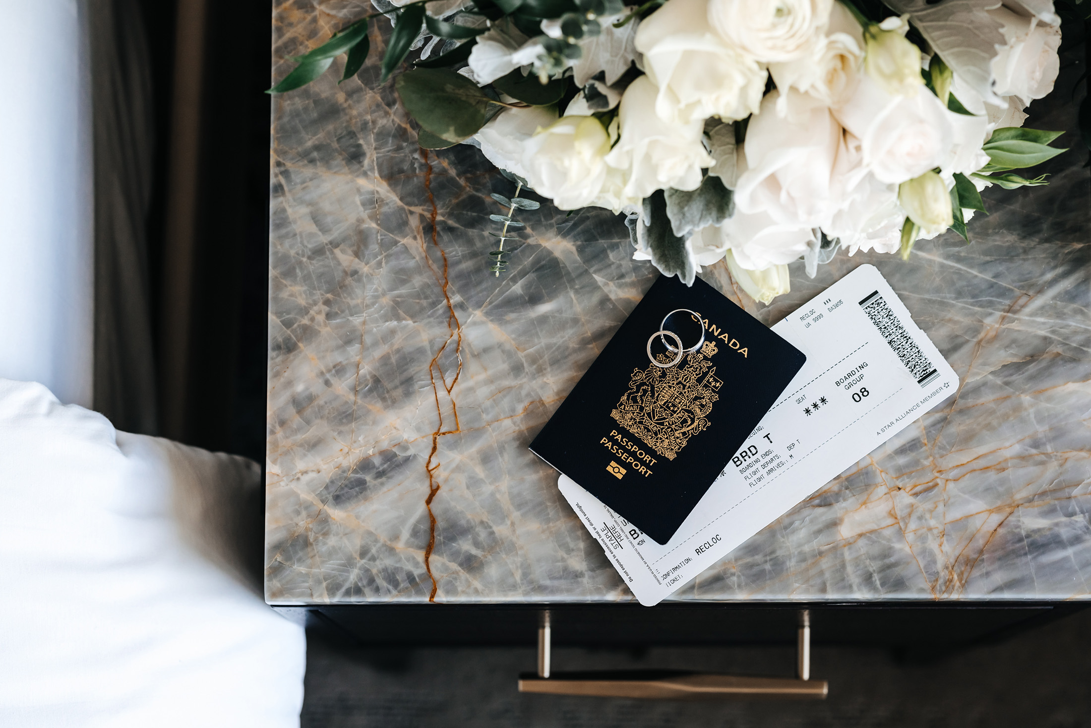 aerial shot of a passport and ticket with two wedding rings and a bouquet of flowers