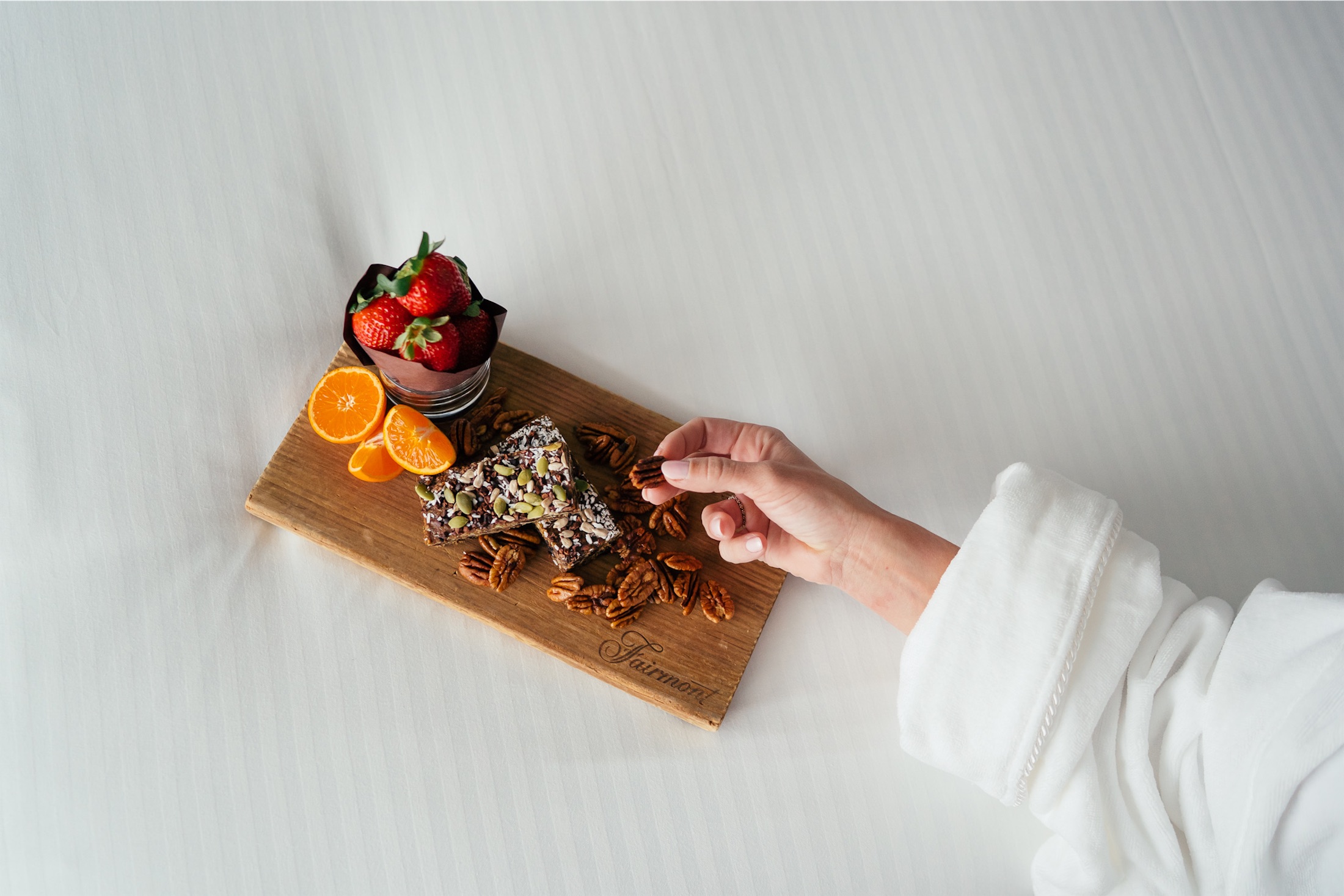 woman picking up a pecan from a small wooden board with breakfast fruit and nuts