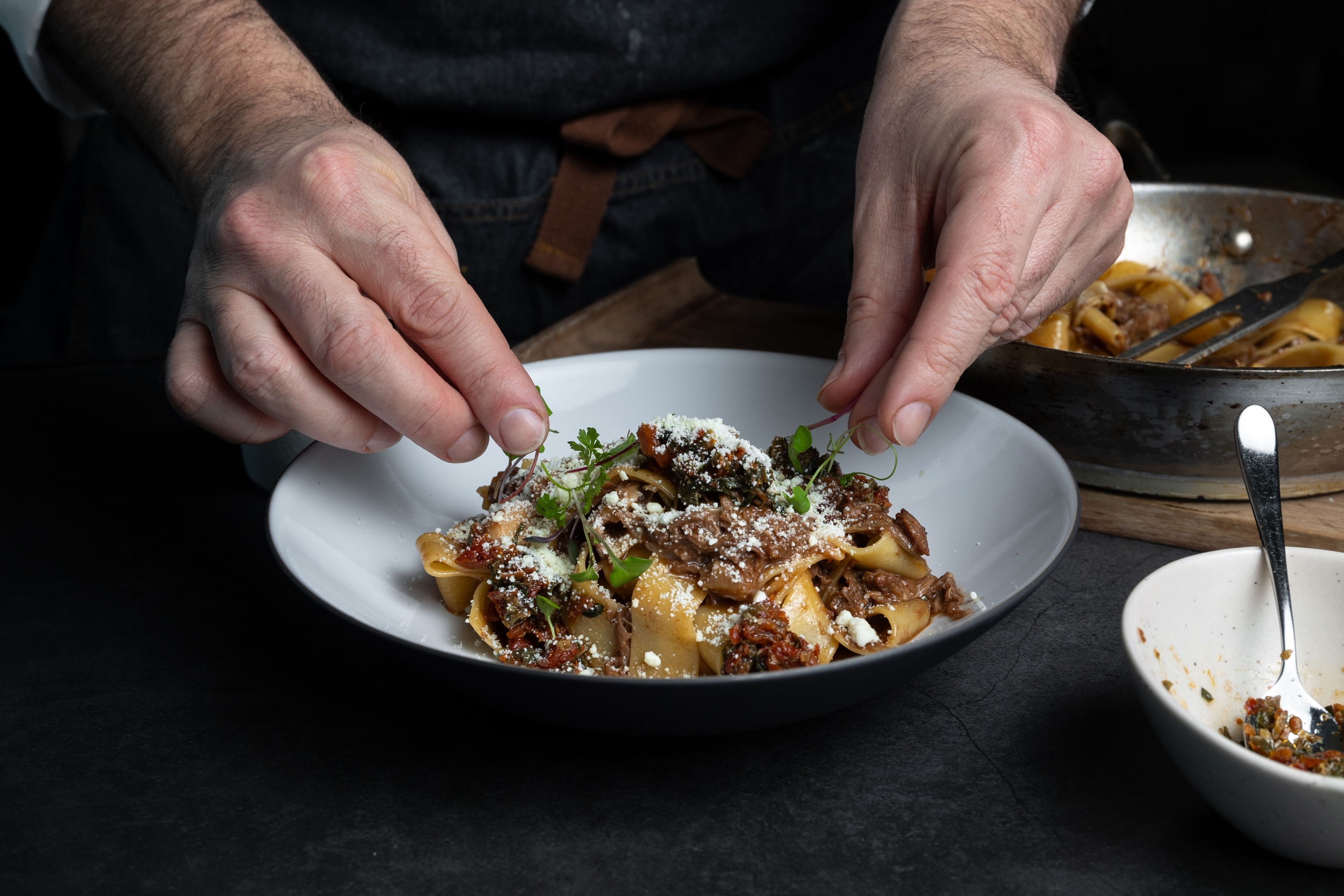 Chef garnishing a bowl of Lamb Pappardelle