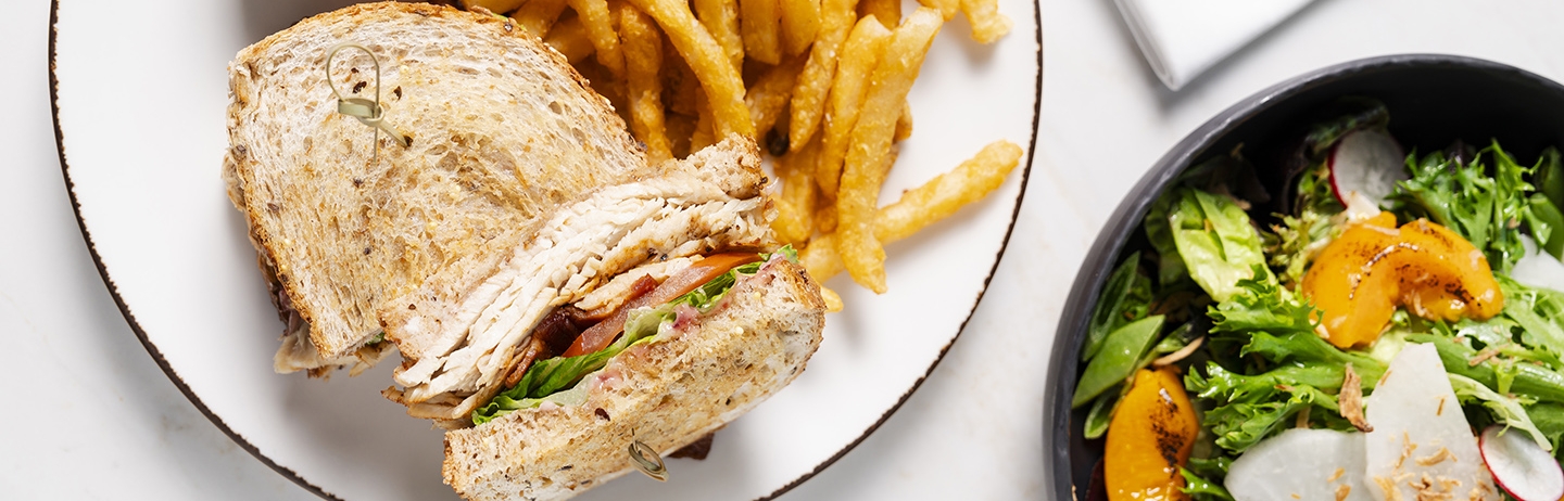 Brightly lit Clubhouse Sandwich with fries and a green salad with charred peaches.