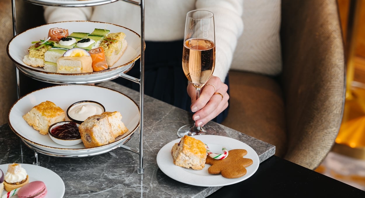 An afternoon tea 3-tier tea tower with pastries, a plate with a gingerbread cookie, and a woman holding a glass of champagne